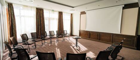 A conference room with a large screen, multiple chairs, and a carpeted floor.