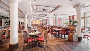 Un restaurante espacioso con techos altos, columnas ornamentales y piso de madera. Mesas y sillas dispuestas para comer.