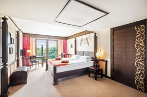 Habitación de hotel con una cama grande, un escritorio y una silla. Tiene un balcón con vistas a zonas verdes.