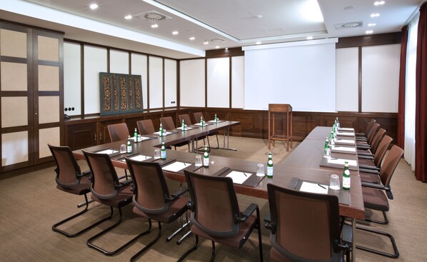 Un salón de conferencias con una larga mesa, sillas y botellas de agua.