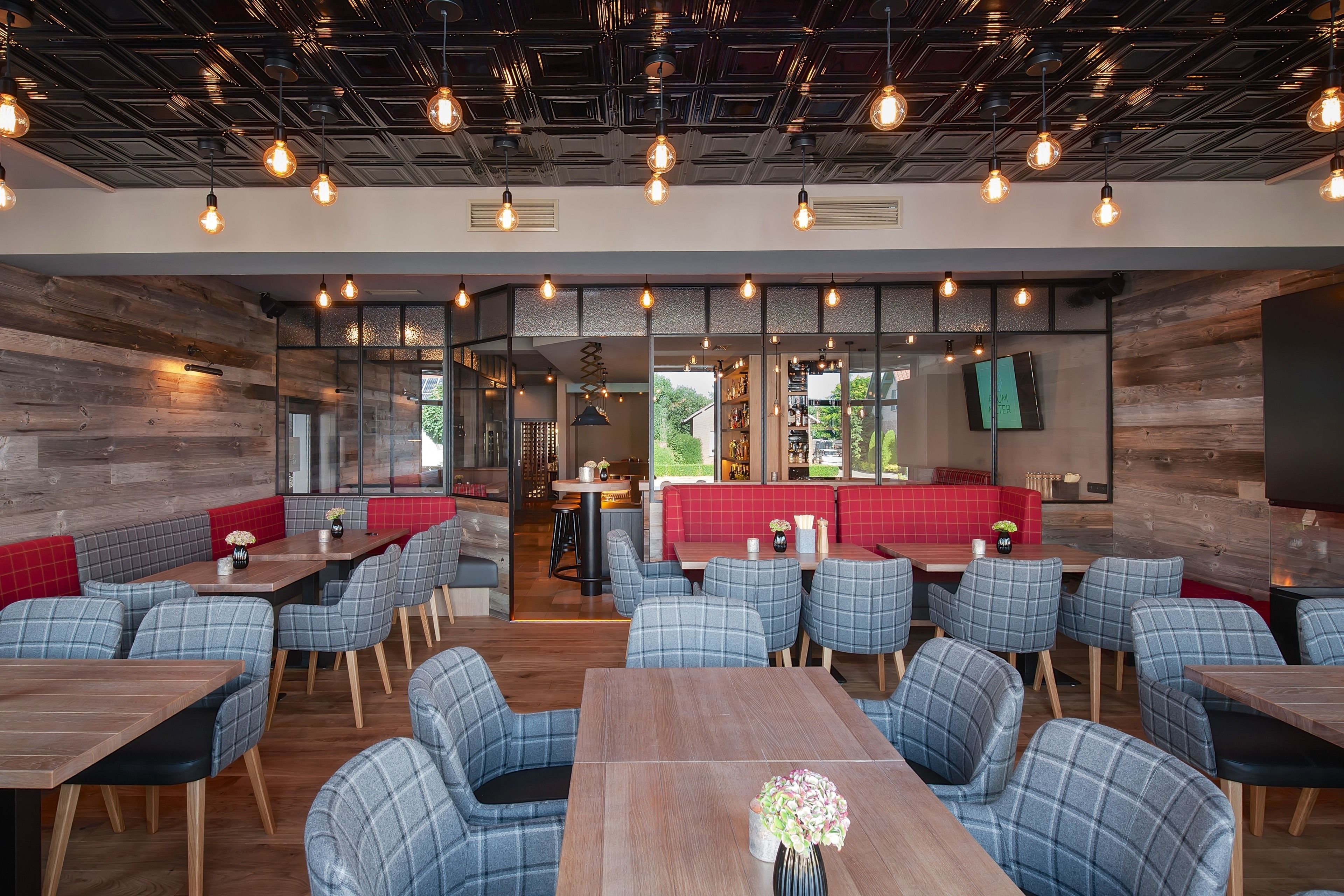Een modern restaurant met geruit zitmeubilair, open verlichtingsarmaturen en uitzicht op het groen.