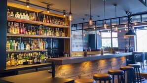 A bar area with shelves of liquor bottles, wooden bar counter, stools, and hanging pendant lights. - Hotel Nickisch (Schuettorf)