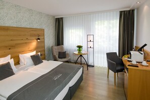 A hotel room with a large bed, a desk with a computer, a chair, and a small table with a plant. - Hotel Nickisch (Schuettorf)