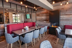 A restaurant with red booths, grey plaid chairs, and a wood-paneled wall with a TV screen. - Hotel Nickisch (Schuettorf)