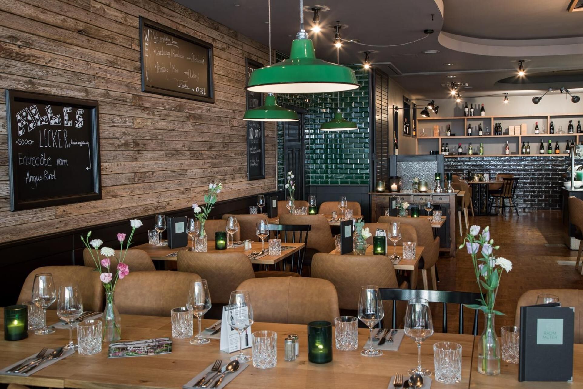 A restaurant interior with wooden walls, green pendant lights, and tables set for dining.