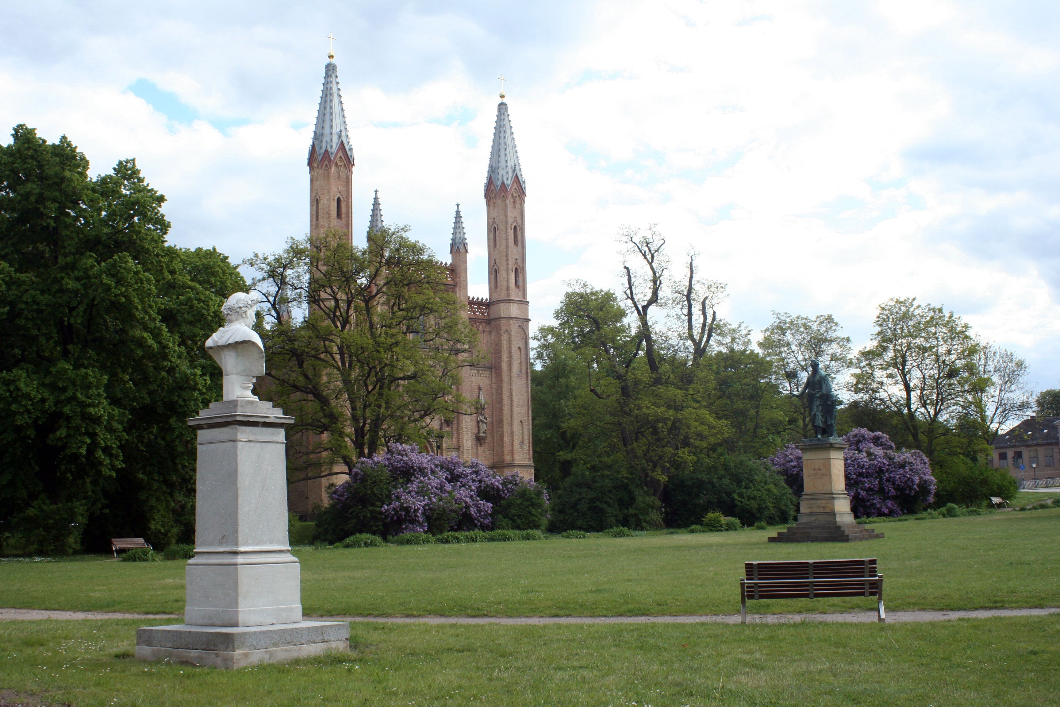 A park with a statue, a bench, and a historic building with towers.
