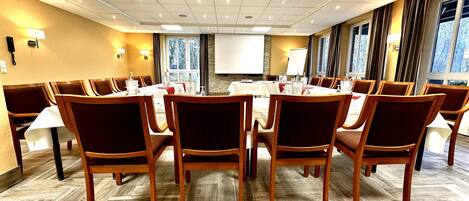 A conference room with a large table, chairs, a projector screen, and windows with curtains.