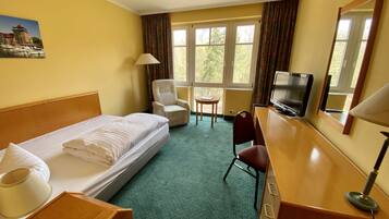 A hotel room with a bed, a desk with a TV, a chair, a small table, and a lamp.