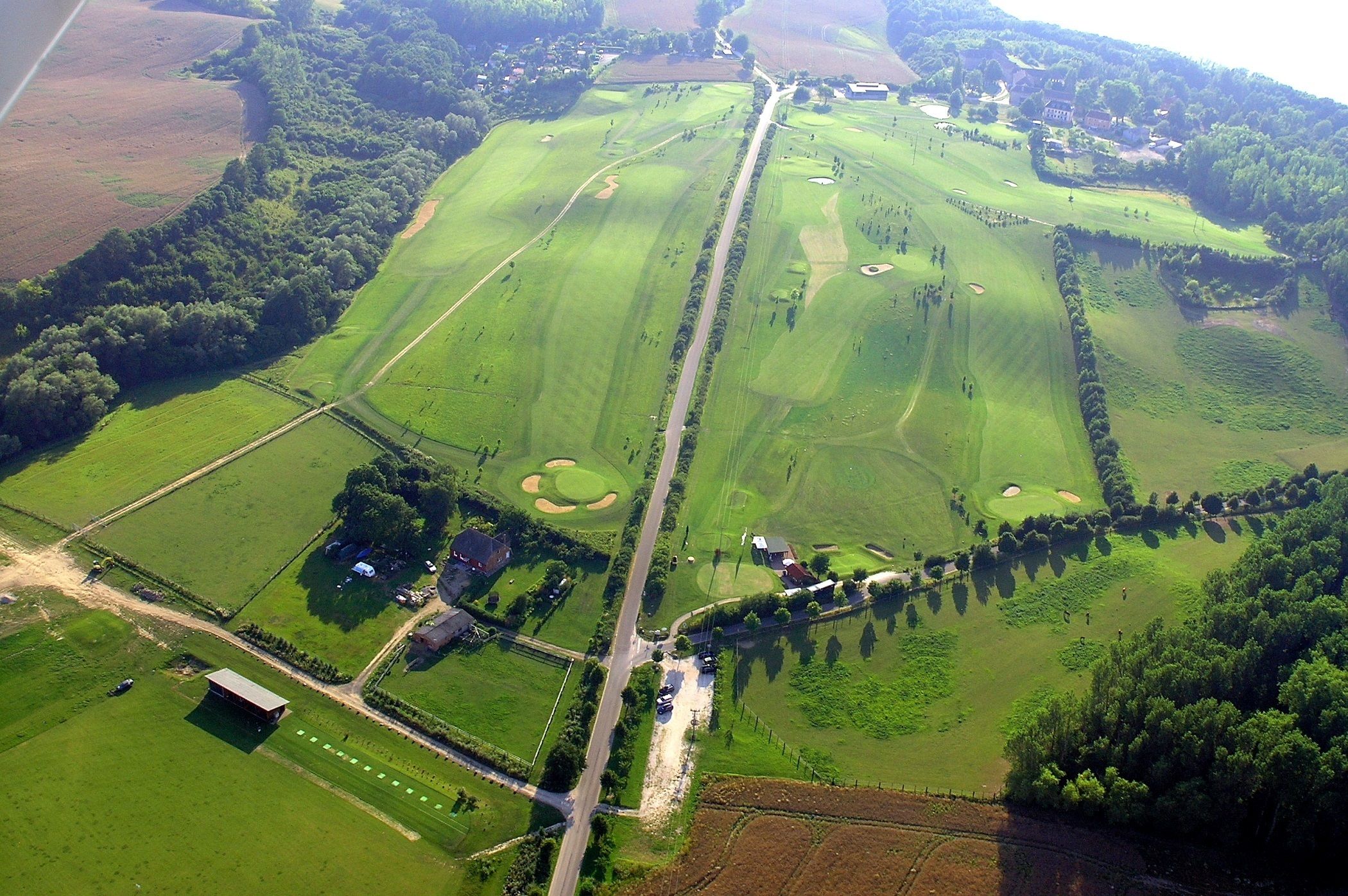 Vista aérea de un campo de golf con múltiples áreas verdes, calles y bunkers de arena.