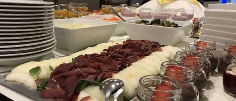 A buffet with various food items including meats, cheeses, and fruits.