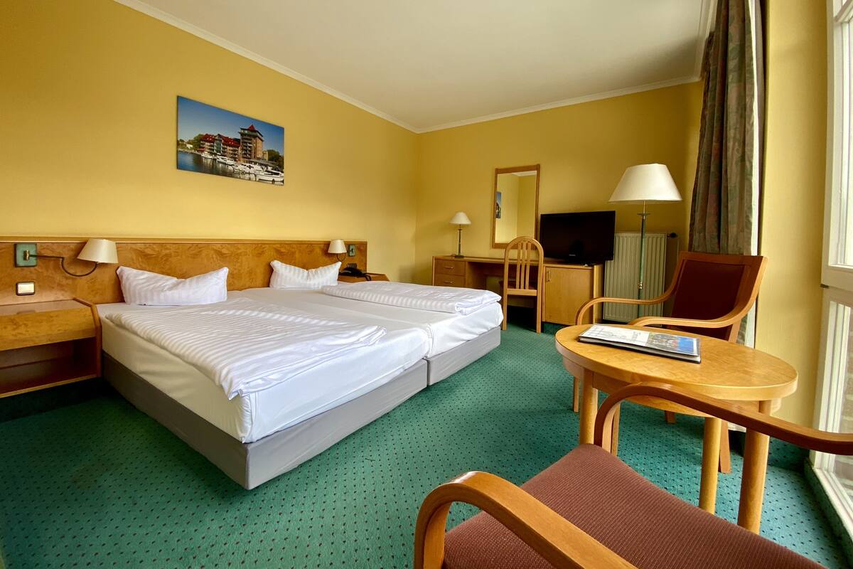 A hotel room with a large bed, a desk, a chair, a TV, and a window with curtains.