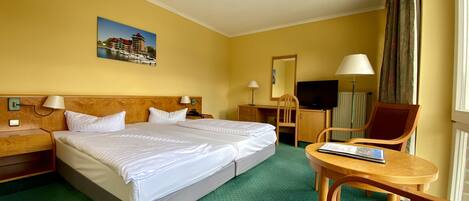Habitación de hotel con una cama grande, un escritorio, una silla, un televisor y una ventana con cortinas.