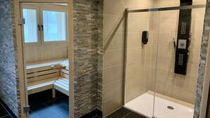 A modern bathroom with a stone wall, a wooden bench, and a glass-enclosed shower area with a control panel. - Park Hotel Fasanerie Neustrelitz (Neustrelitz)