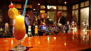 A bar with a glass of orange juice garnished with a cherry and a straw, and bottles of alcohol in the background. - Park Hotel Fasanerie Neustrelitz (Neustrelitz)