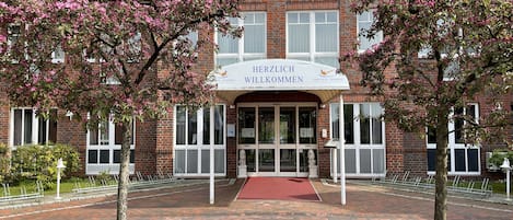 A hotel entrance with a red carpet, brick facade, and a sign reading "HERZLICH WILKOMMEN".