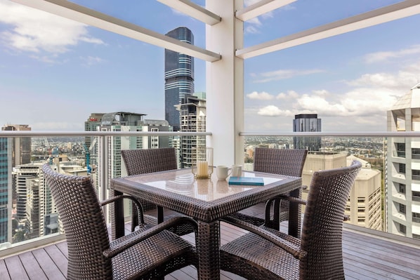 A balcony with wicker furniture, a glass table, and a view of the cityscape. - Oaks Brisbane Casino Tower Suites (Brisbane)