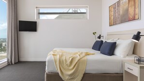 Habitación de hotel moderna con una cama grande, un televisor de pantalla plana en la pared, una ventana con vistas a un puente y un cuadro sobre la cama.