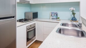Una cocina compacta con gabinetes blancos, un refrigerador de acero inoxidable, un microondas, una estufa a gas y un lavamanos doble.