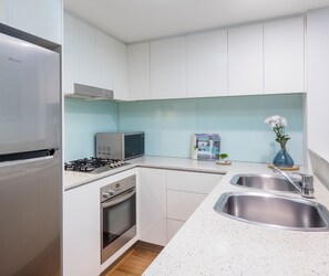 A compact kitchen with white cabinets, a stainless steel refrigerator, a microwave, a gas stove, and a double sink.