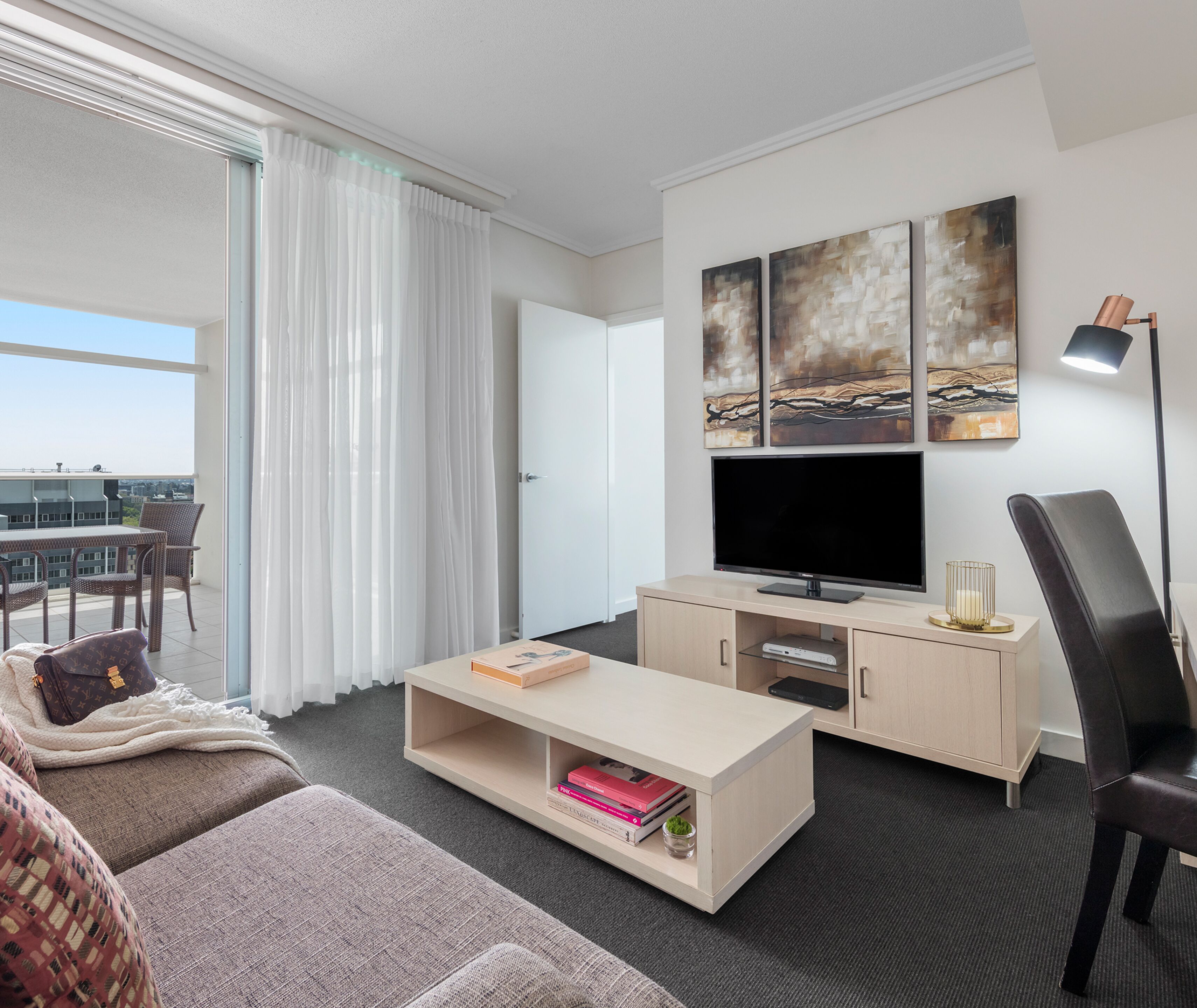 Quarto de hotel moderno com uma televisão de tela grande, um sofá, uma mesa de centro e uma área de trabalho.