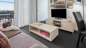 Una habitación de hotel moderna con un televisor de pantalla plana grande, un sofá, una mesa de centro y una zona de trabajo.