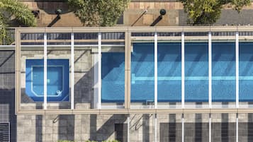 Un edificio con una piscina grande, un jacuzzi más pequeño y un área techada con asientos.