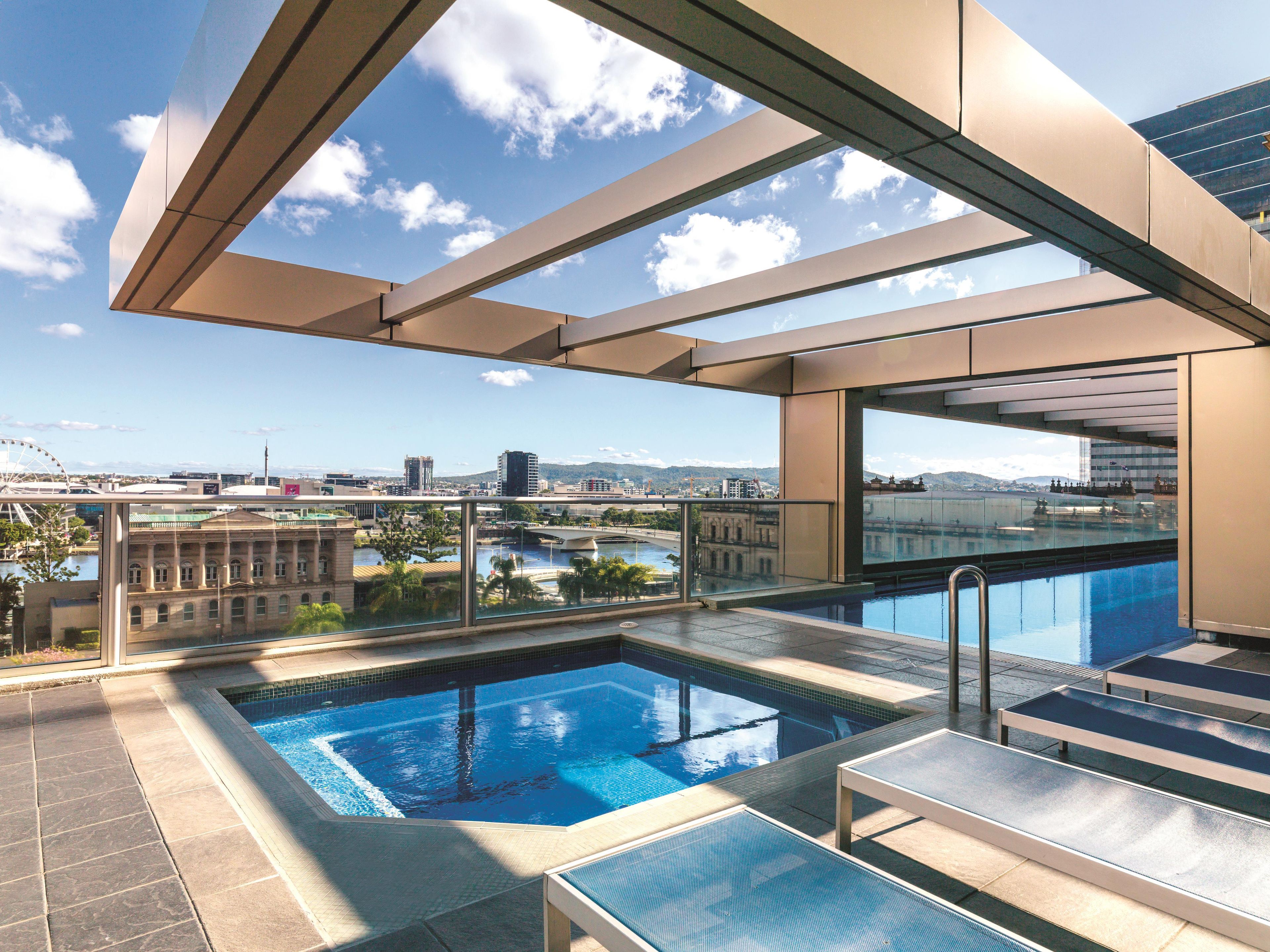A rooftop pool with clear views of a cityscape, including a bridge and buildings.