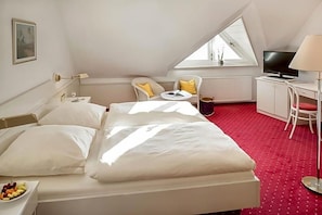 A hotel room with a bed, a desk, a chair, a television, and a window.