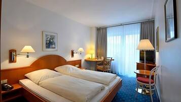 A hotel room with a double bed, bedside lamps, a desk with a chair, a television, and a large window with curtains.