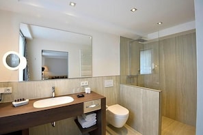 A modern bathroom with a wooden vanity, a large mirror, a toilet, and a glass-enclosed shower area.