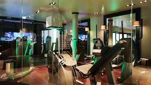 Un gimnasio con equipo de ejercicio, un espejo grande y una zona de recepción con televisión.