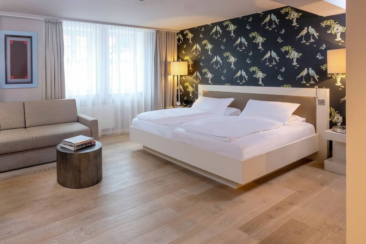 A hotel room with a bed, a sofa, a desk, and a chair.