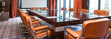 A conference room with a long table, multiple chairs, and a projector screen.