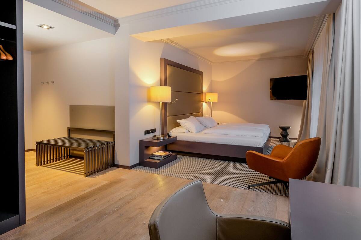 A hotel room with a bed, bedside lamps, a TV, a desk, and a chair.