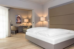 A hotel room with a bed, two bedside lamps, a desk with a chair, and a painting on the wall. - Zum Löwen Design Hotel Resort & Spa (Duderstadt)