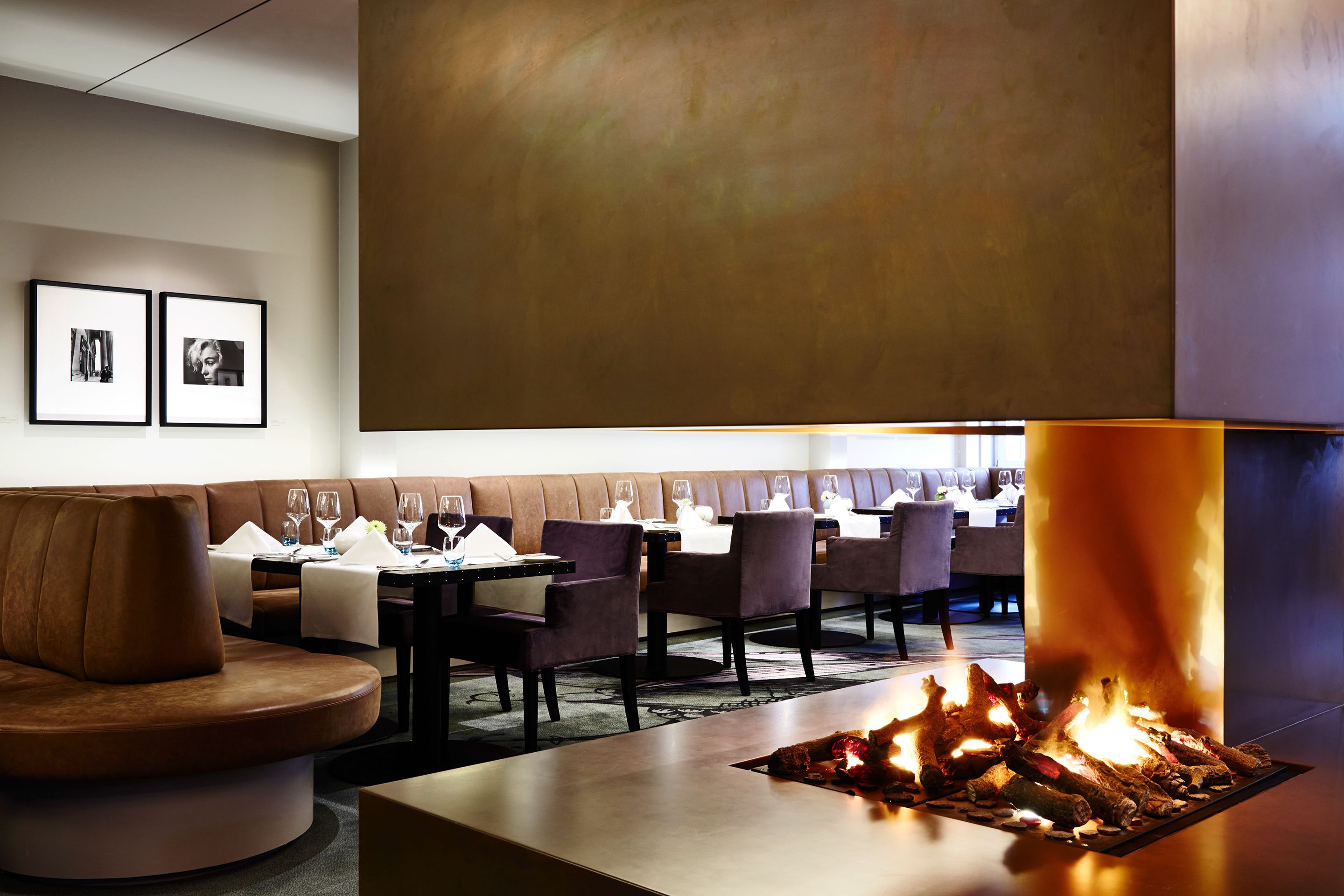 A modern dining area with a central fire feature, seating arrangements, and framed artwork on the wall.