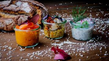 Three glass jars with food items, a loaf of bread, and scattered white grains on a wooden surface.