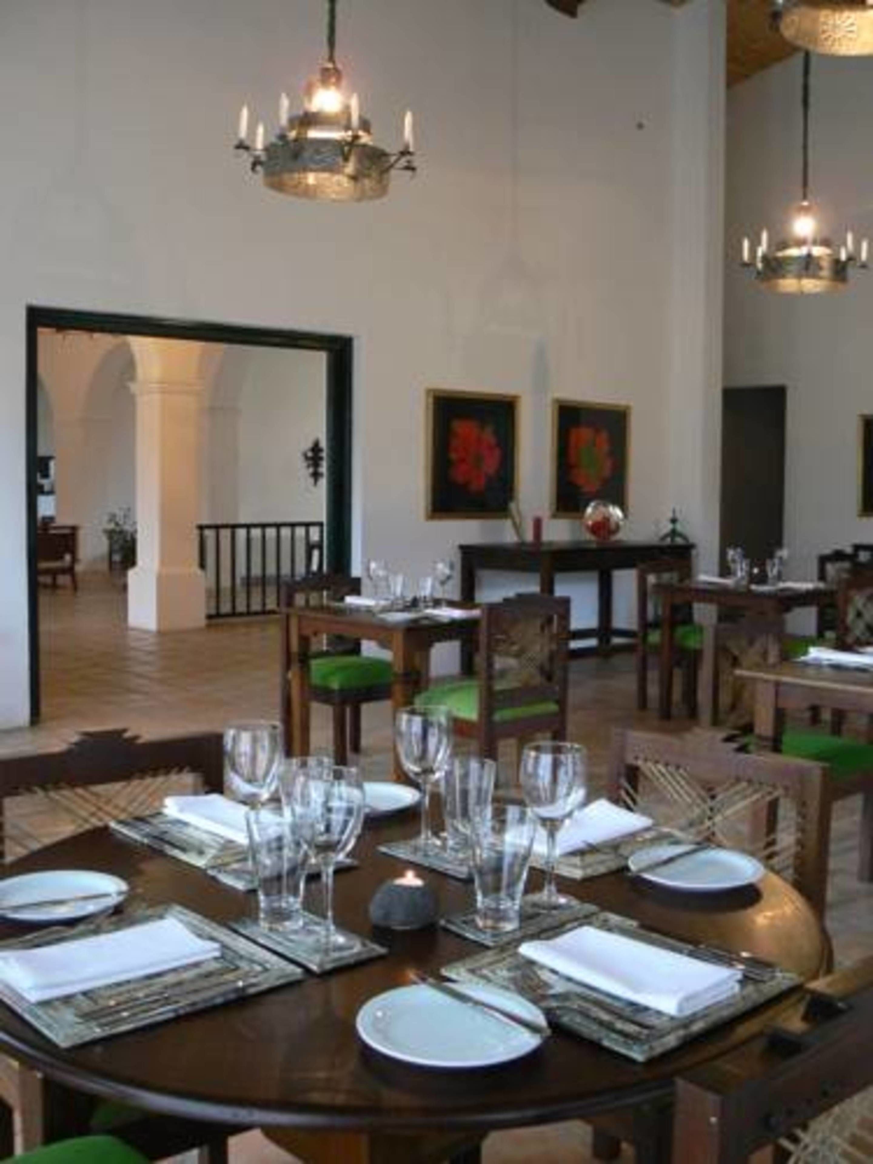 Un comedor con mesas redondas dispuestas para una comida, con sillas que tienen cojines verdes y una araña colgando del techo.