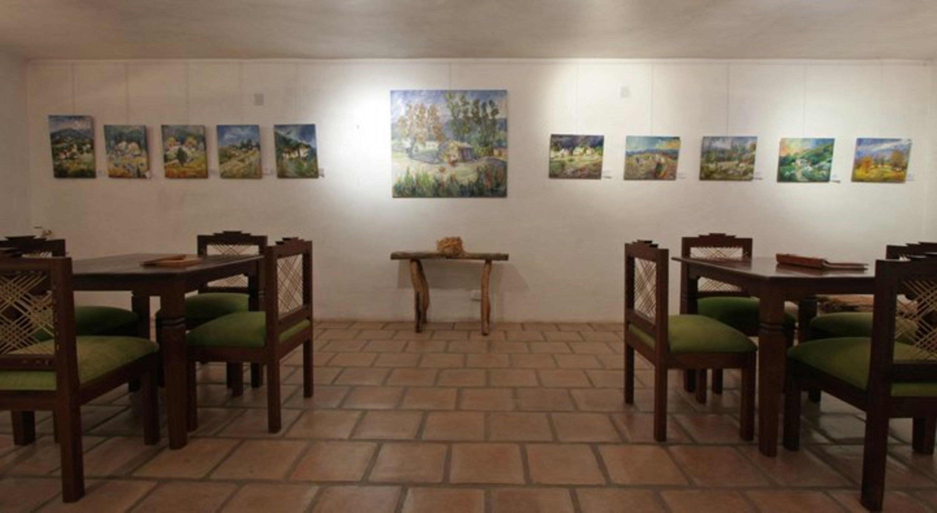 Un comedor con mesas y sillas de madera, una mesa central pequeña y varias pinturas de paisajes en las paredes.