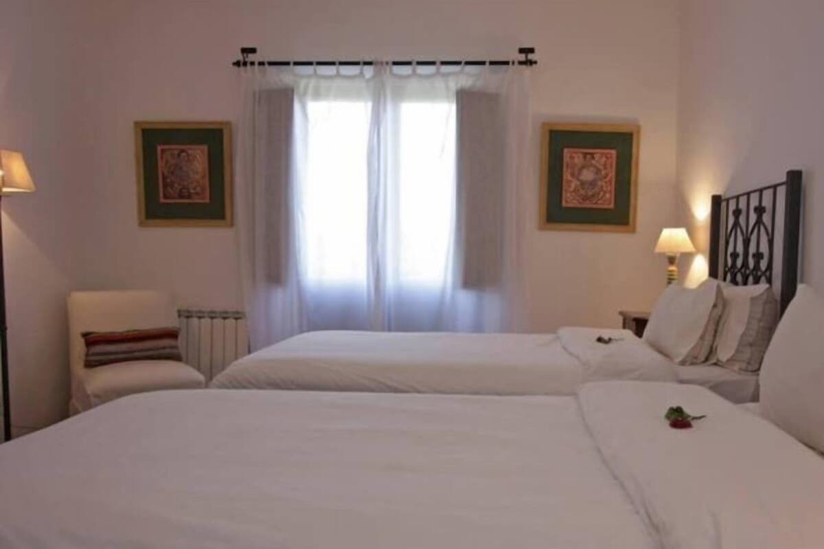 A double room with two beds, a radiator, a window with curtains, and two wall-mounted lamps.