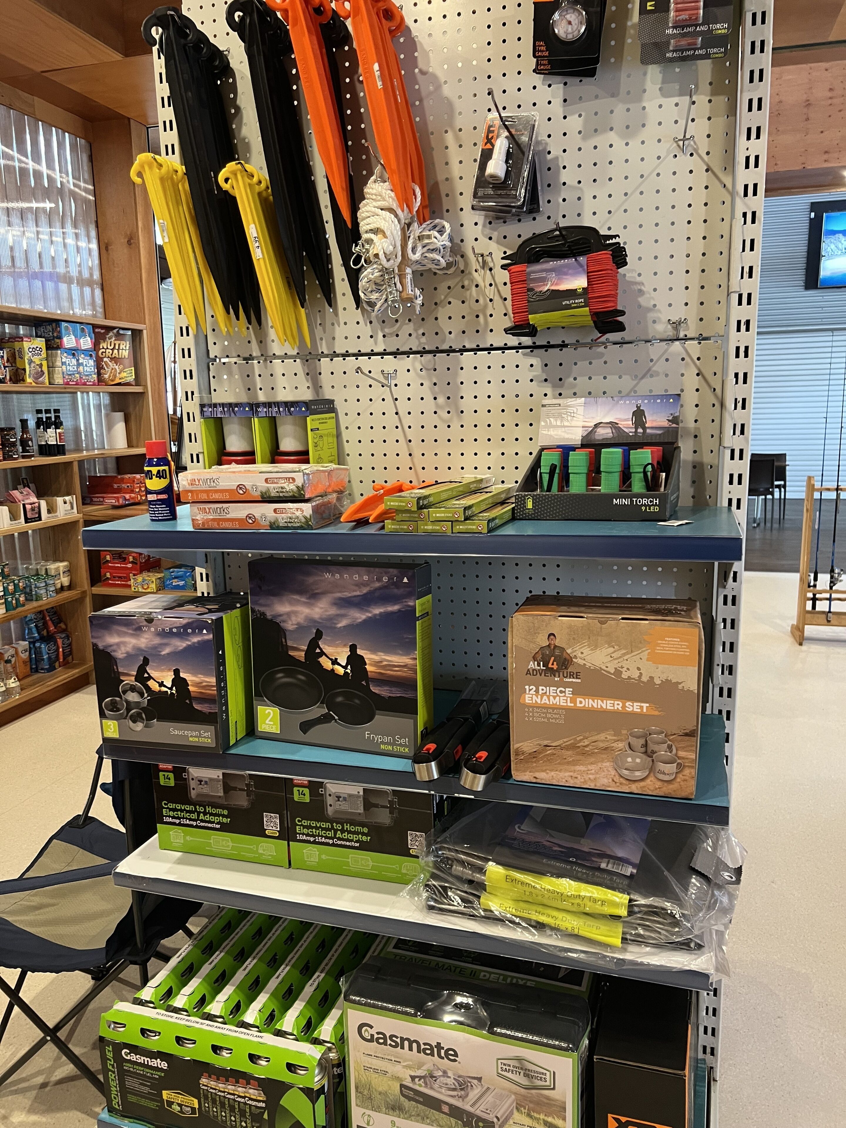 Udstilling af camping- og udendørsudstyr i butik, herunder pandelamper, lommelygter og et transportabelt komfur.