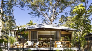 A treehouse with a covered porch, outdoor furniture, and a view of the surrounding forest. - Noosa North Shore Retreat (Noosa North Shore)