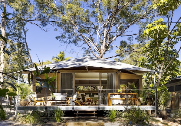 Una casa en los árboles con un porche cubierto, mobiliario exterior y vistas al bosque circundante.