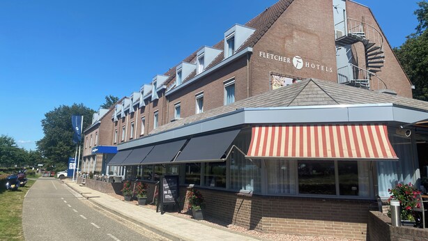 A hotel with a brick facade, a red and white awning, and a visible staircase leading to the roof.