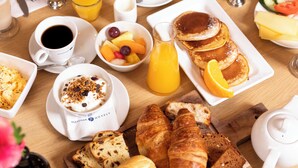 A breakfast table with croissants, pancakes, fruit, coffee, and juice.