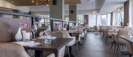 Un restaurant spacieux, doté de nombreuses tables et chaises, de grandes fenêtres et d’un décor moderne.