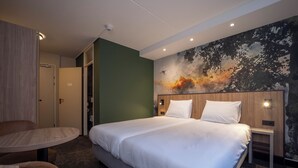 A hotel room with a large bed, a round table, and a chair. There is a painting on the wall and a door leading to another room.