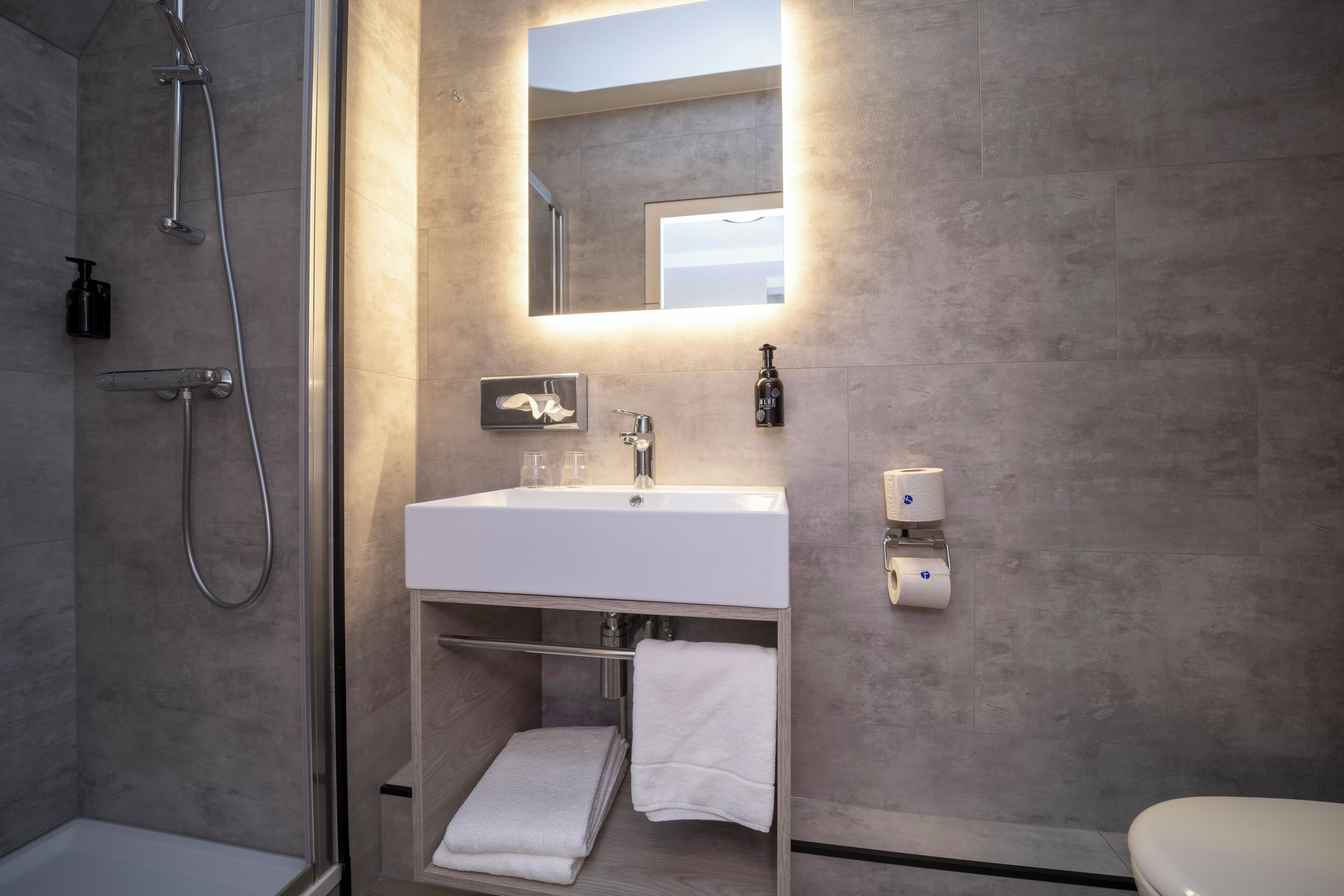 A modern bathroom with a glass-enclosed shower, a white sink with a mirror above, and a toilet.