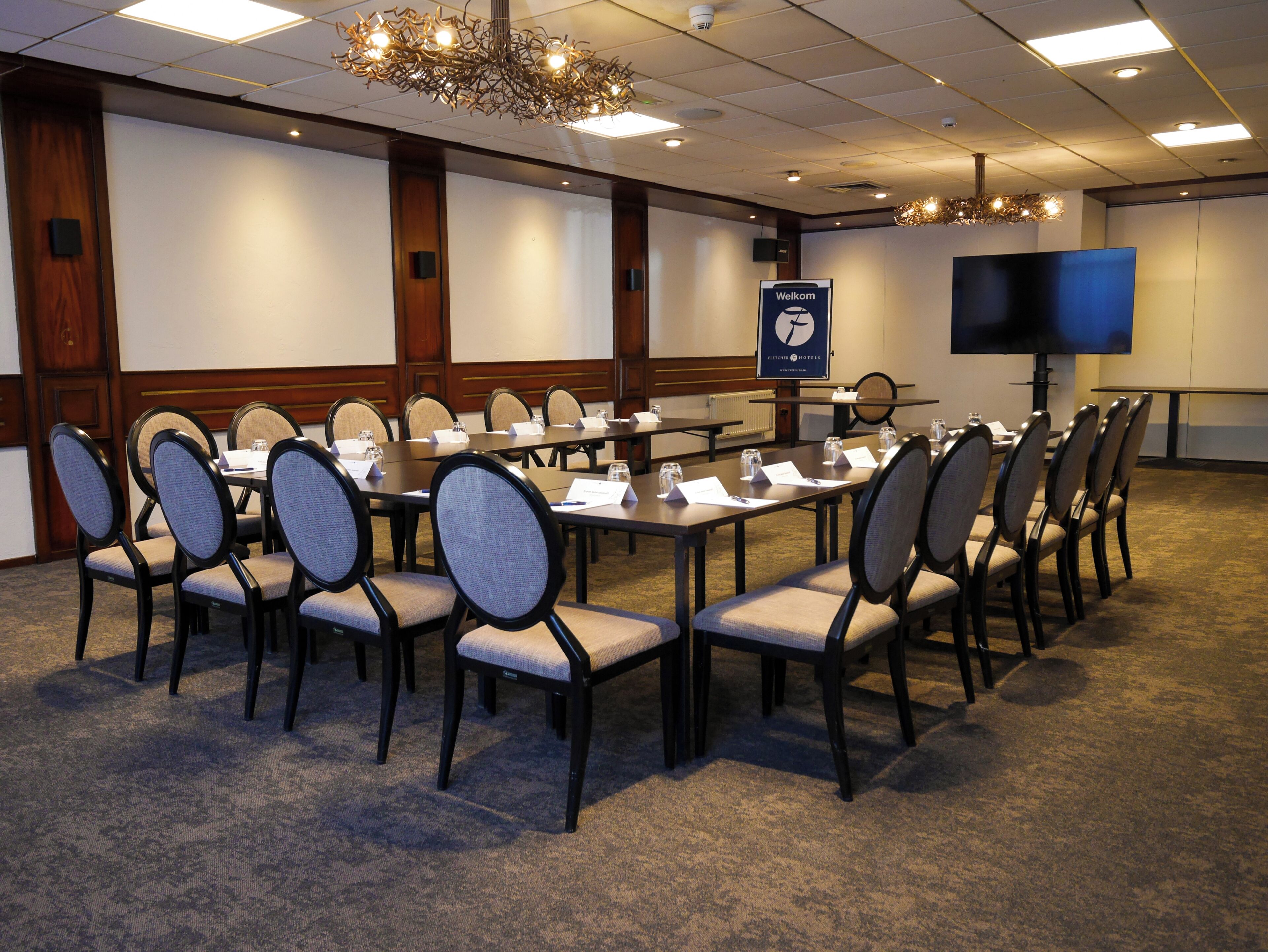 A conference room with multiple tables and chairs, a large screen, and a 'Welcome' sign.