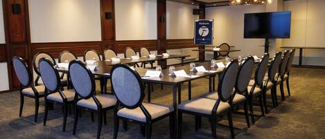 A conference room with multiple tables and chairs, a large screen, and a 'Welcome' sign.
